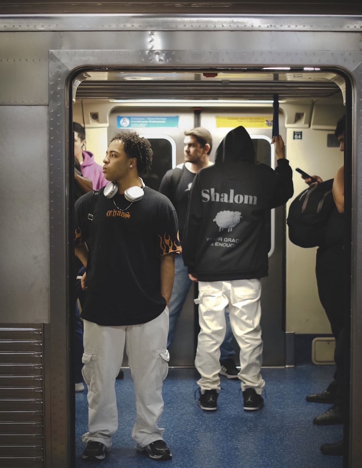 Jovens no metrô — um com camiseta preta de chamas laranja e outro com moletom preto SHALOM Your Grace is Enough